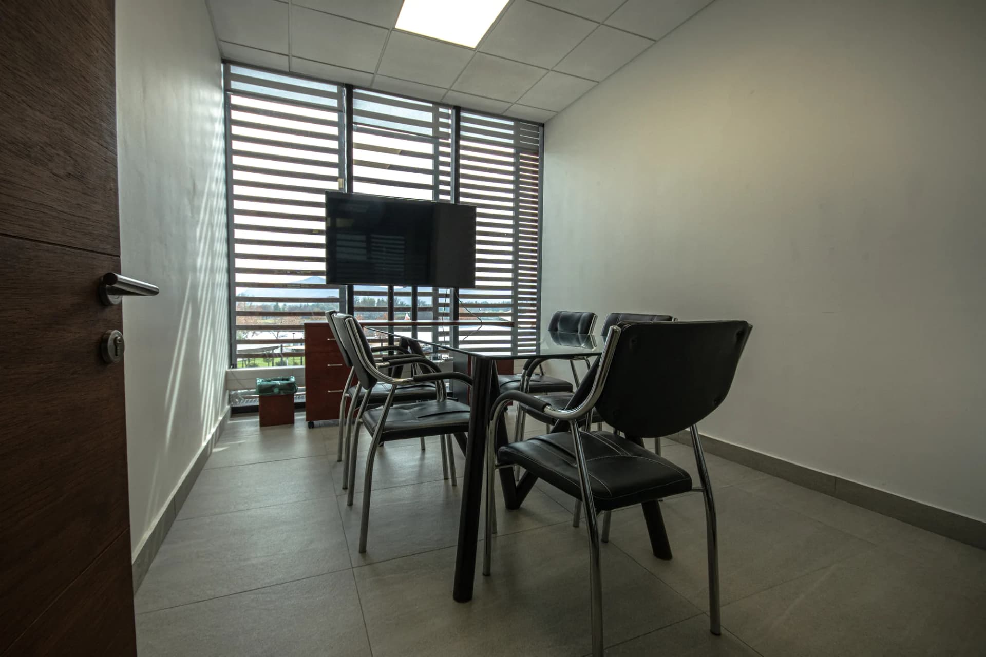 Sala de reunión chica con TV y ventanal con celosías